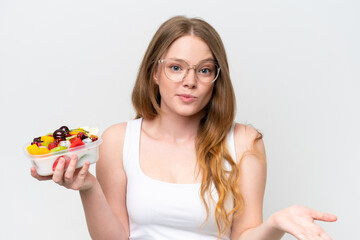 Young pretty woman holding a bowl of fruit isolated on white background making doubts gesture while lifting the shoulders