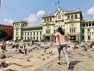 Guatemala City, Guatemala / Guatemala - CERCA 2020: Girl chasing pigeons in front of the National Palace at the historic center, zone 1
