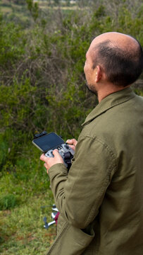 Imagen de un hombre calvo de espalda pilotando un dron con control remoto en las manos, mirando el cielo y naturaleza de fondo con vegetacion verde