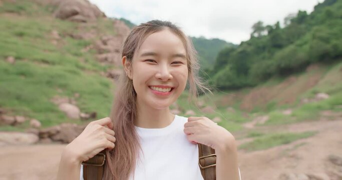 Attractive asian woman hiker smiling with confident and happy emotion. Close up portrait of young beautiful female with backpack looking to camera enjoying nature in forest trail mountain background.
