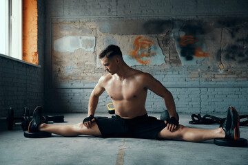 Fototapeta na wymiar Confident young man doing the splits while exercising in gym