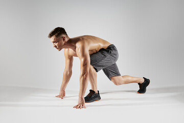 Young fit man preparing to run while standing in starting position against white background - obrazy, fototapety, plakaty