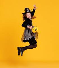 Happy girl in  witch costume with pumpkin basket jumping and celebrates Halloween on yellow...