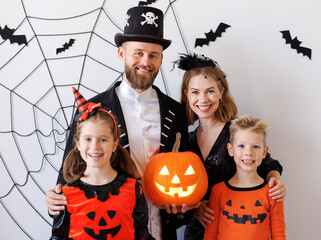 Cheerful family   in carnival costumes celebrate Halloween near  a gray wall with cobwebs and bats