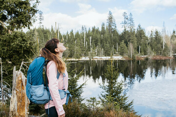Fototapeta na wymiar A young girl with a sports backpack on her back enjoys nature. A woman stands and inhales clean forest air