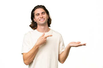 Young caucasian man isolated on green chroma background holding copyspace imaginary on the palm to insert an ad
