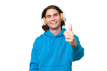 Young handsome man isolated on green chroma background listening music and with thumb up