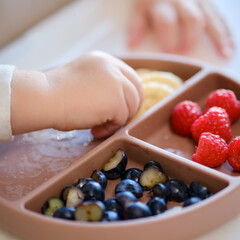 Obraz na płótnie Canvas Toddler baby eats fruits and berries with his hand, table close-up. Child hands take food from a beige plate. Kid aged one year and two months