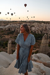 Fototapeta premium Tourist girl standing and looking to hot air balloons in Cappadocia, Turkey. Happy Travel in Turkey concept. Woman on a mountain top enjoying wonderful view. High quality photo