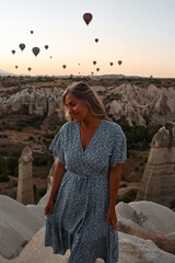 Tourist girl standing and looking to hot air balloons in Cappadocia, Turkey. Happy Travel in Turkey concept. Woman on a mountain top enjoying wonderful view. High quality photo