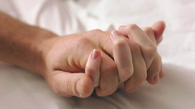 Couple, love and trust holding hands while in bed bonding, lying and touching with a wedding ring on wife sharing intimacy, support and commitment in marriage. Closeup of man and woman on honeymoon