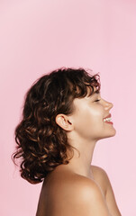 Profile photo of young female model, curly hair, closed eyes, laughing, advertising of skin care treatment, cosmetic and spa product on pink background
