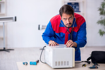 Young male repairman repairing oven at workshop