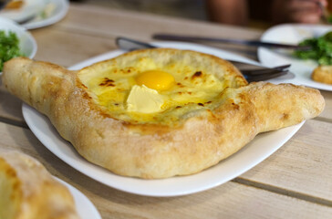 Beautiful open khachapuri pies with egg and butter on a white plate.
