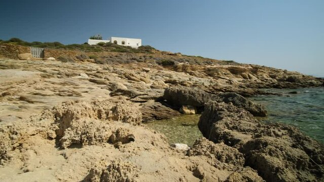 View of a small chapel, a whitewashed villa and the rocky beach of Magganari in Ios Greece