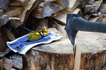 Axe for separation of parts in crack of wooden cylinder and protective glasses and gloves on stump, harvesting firewood for heating season in winter