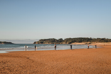 Fototapeta na wymiar group of surfers on the beach as they prepare to enter the water for surfing during a surf and travel week experience in Somo, Cantabria (Spain)