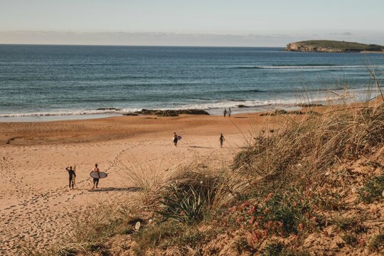 group of surfers walk on the beach with their surfboards in the direction of the sea during a surf and travel week experience in Somo, Cantabria (Spain)