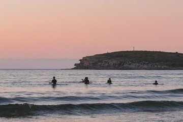 group of surfers in the sea with the board while waiting for the arrival of the waves at sunset during a surf and travel week experience in Somo, Cantabria (Spain)