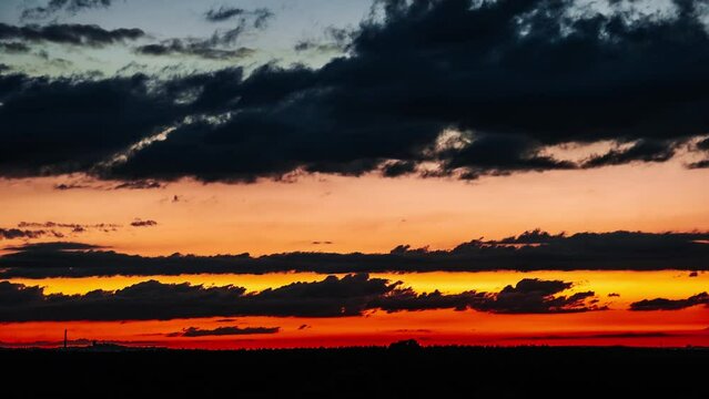 Clouds after sunset in the orange colorful sky. Vibrant gold-colored twilight cloudscape. Scenic time lapse of a vibrant red and orange sky as the dark clouds light up with color during sunset. 4K