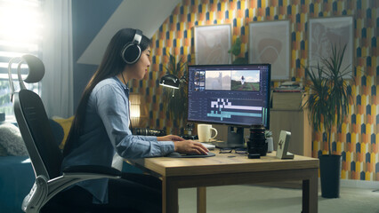Asian woman sitting at the desk in headphones at home office and editing video for blog in...