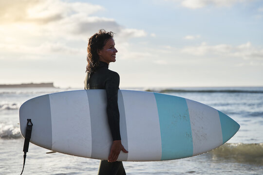 Surfer girl feeling happy with her board on the sandy beach