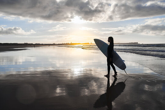 Silhouette of the surf woman walking with her board at seashore at the sunset
