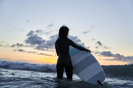 Woman silhouette holding surf board at the ocean and looking away