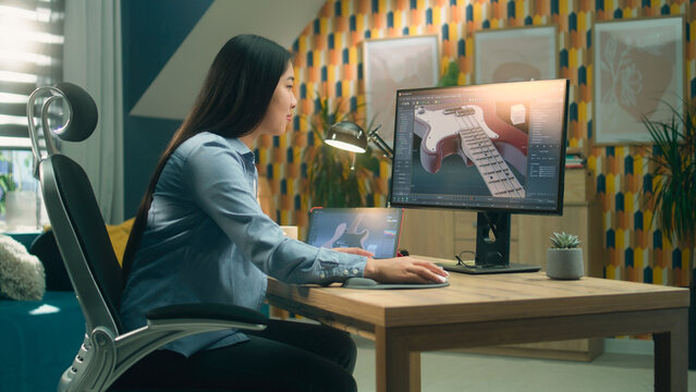 Asian woman designing 3D prototype of electric bass guitar using modern personal computer and tablet in 3D modeling program while working remotely from home