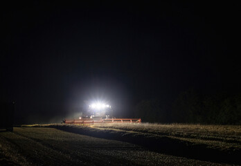 Combine harvester working at night with front headlights illuminating the field during the last...