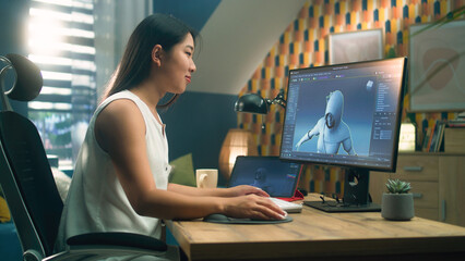 Asian woman creating 3D model of video game character in professional program using computer and...