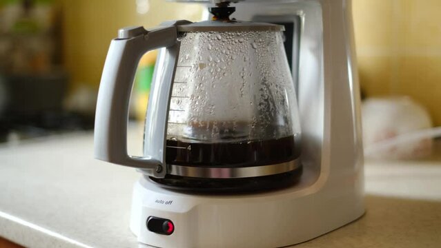 Droplets of brewed coffee drip slowly into the coffee pot mounted on the platform of a black coffee maker