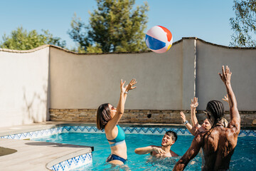 multi-ethnic group playing in a swimming pool with a ball