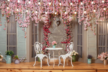 two white chairs and a table against the backdrop of decorations with pink flowers. photo zone with pink sakura flowers in a photo studio. decorative entrance to the house with furniture and a door. © Yashkin Ilya