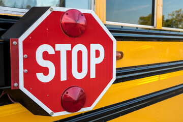 A red stop sign with lights on the side of a yellow school bus.