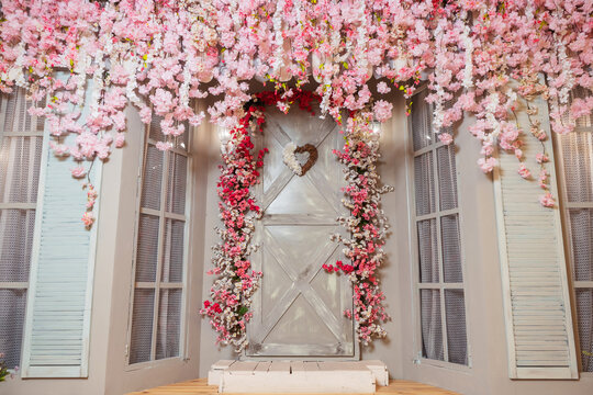 veranda with gray door and pink flowers. photo zone with pink sakura flowers in a photo studio. decorative entrance to the house with furniture and a door.