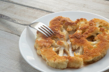 Close-up of fried cauliflower schnitzel on a plate on a wooden table. The concept of vegetarianism.