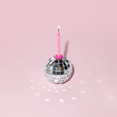 Shiny disco ball and candle on pastel light pink background. Minimalistic party concept. Creative birthday composition.