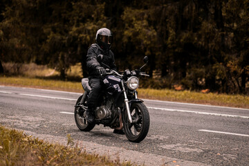 motorcyclist in a motorcycle jacket and a helmet with a sun visor on a custom motorcycle cafe racer. Stylish motorcyclist and autumn road.