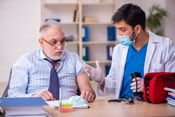 Young male doctor visiting old businessman at workplace