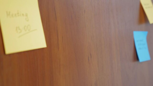 The girl unsticks a sticker on the wall with a plan for the day. A close-up woman's hand unhooks a note with a to-do list.