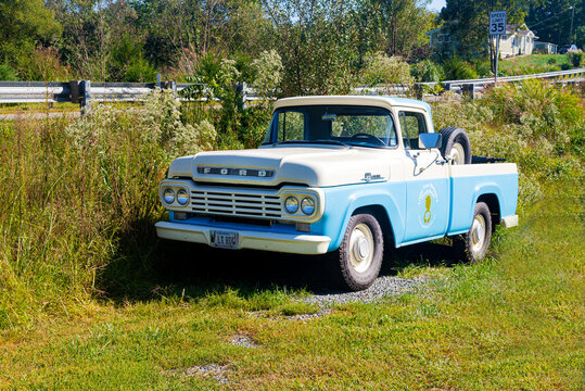 Ford F100 antique pickup truck parked in a farm field along the roadside blue.