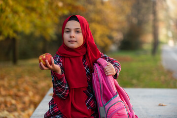A Muslim child girl in fashion hijab eating healthy breakfast outdoors on the school lunch.
