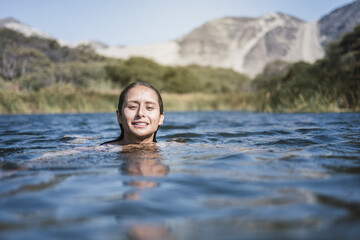 Beautiful latin young woman bathes in a lake. It stands at the bottom of the shoulders in the water. She is happy and smiling relaxing on a beautiful summer day