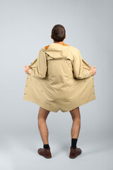 Exhibitionist exposing naked body under coat on light background, back view