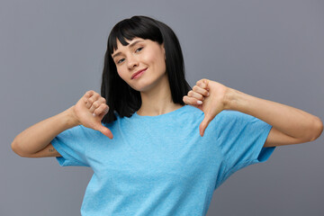 a lovely woman stands on a gray background in a blue T-shirt, happily grinning, stretching her hands a little in front showing dislike