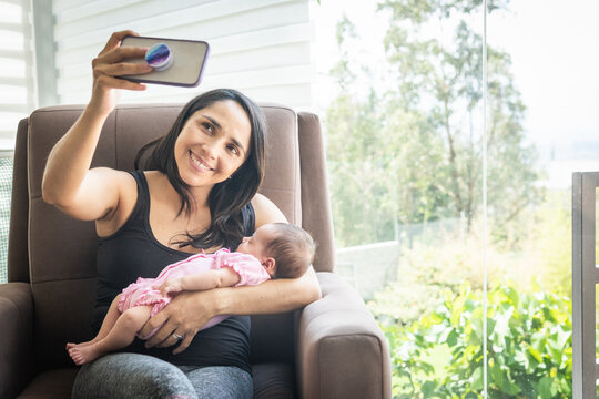 Young woman taking a selfie sitting on a sofa with her baby at home