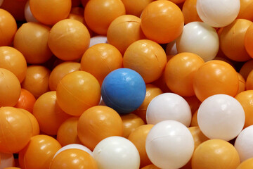 1 blue ball among many orange and white balls. Selective focus