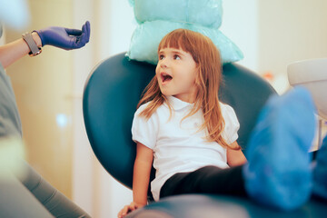 Happy Toddler Girl Sitting in a Dental Chair for Routine Visit. Little child visiting a pediatric...