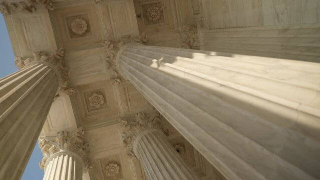 Turning view looking up at the top of Corinthian columns in front of US Supreme Court in Washington, DC, showing chaos of power over people and business.